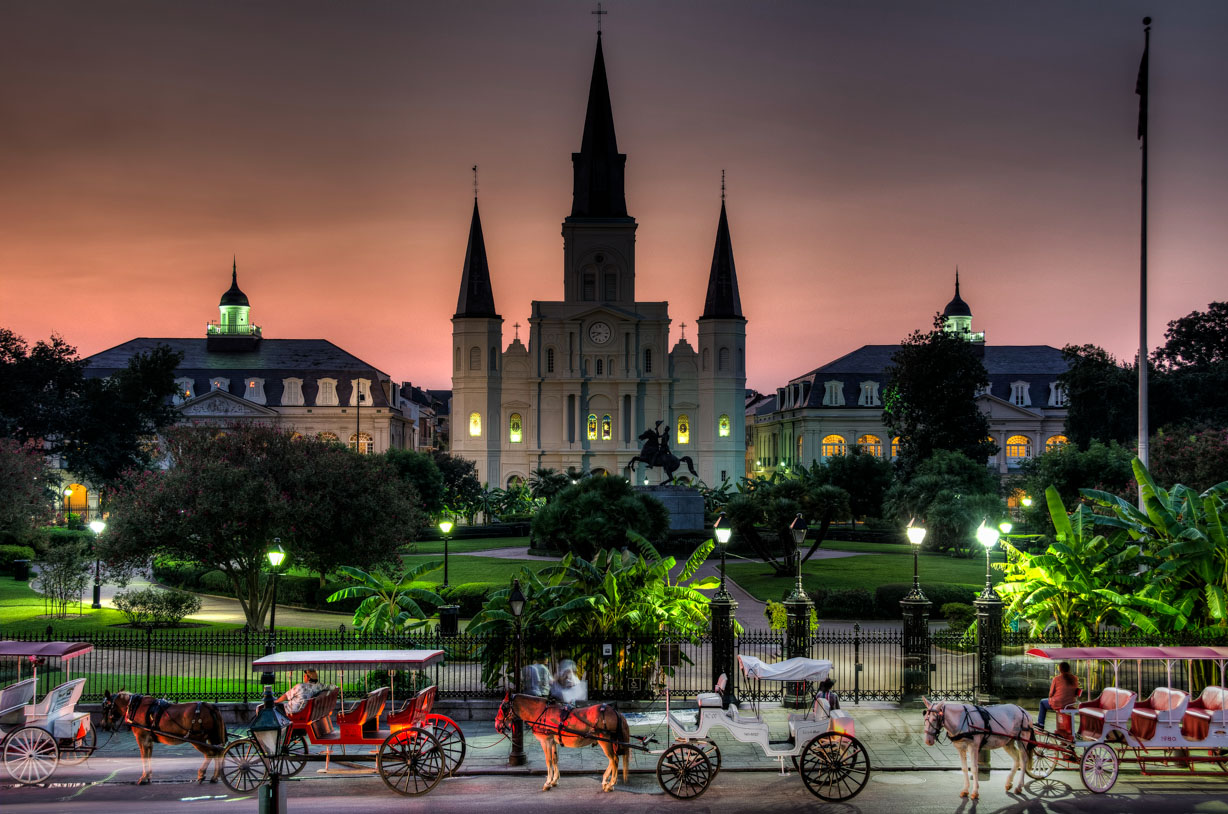 Nighttime view of Jackson Square, New Orleans, bathed in the warm glow of street lamps with St. Louis Cathedral illuminated in the background.